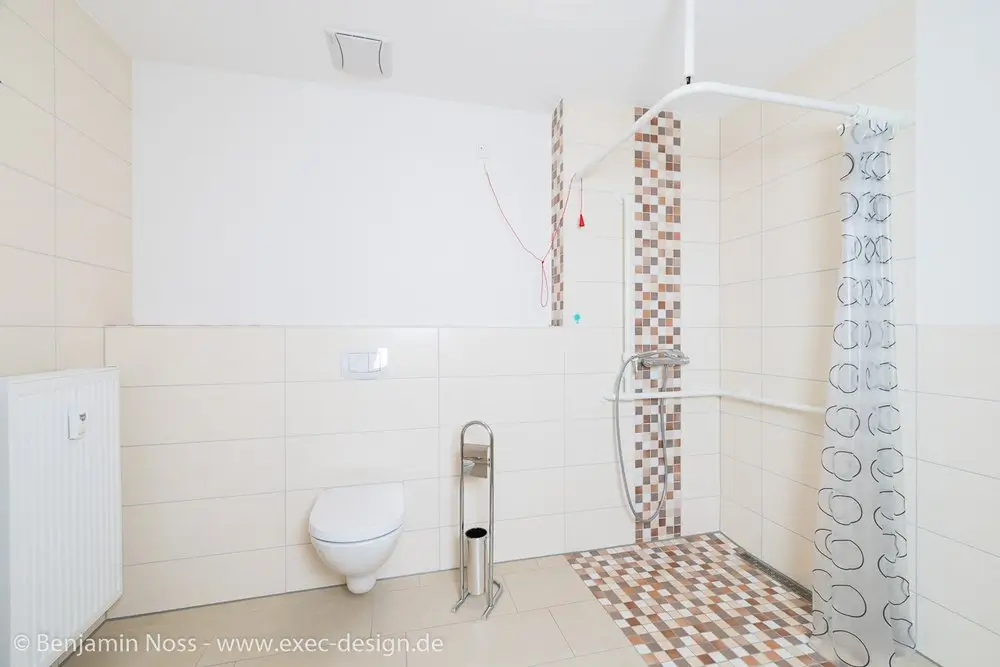 Helles Badezimmer mit wandhängendem WC, Duschbereich mit Mosaikfliesen und Duschvorhang mit Kreis-Muster