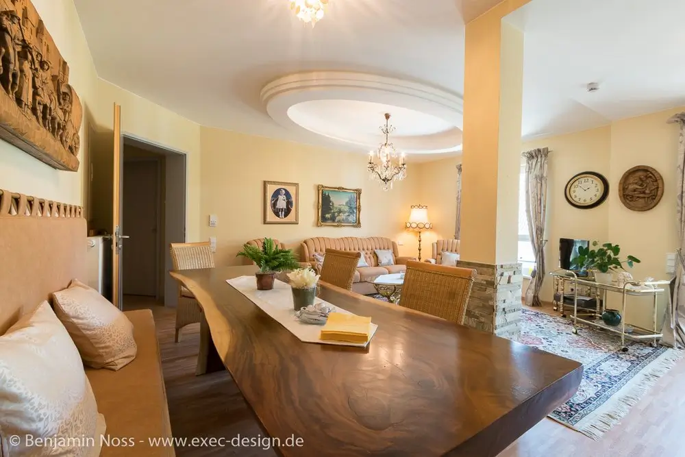Wohnzimmer mit großem, naturbelassenem Holzesstisch, Rattanstühlen, Sofa, Teppich und Wanddekoration