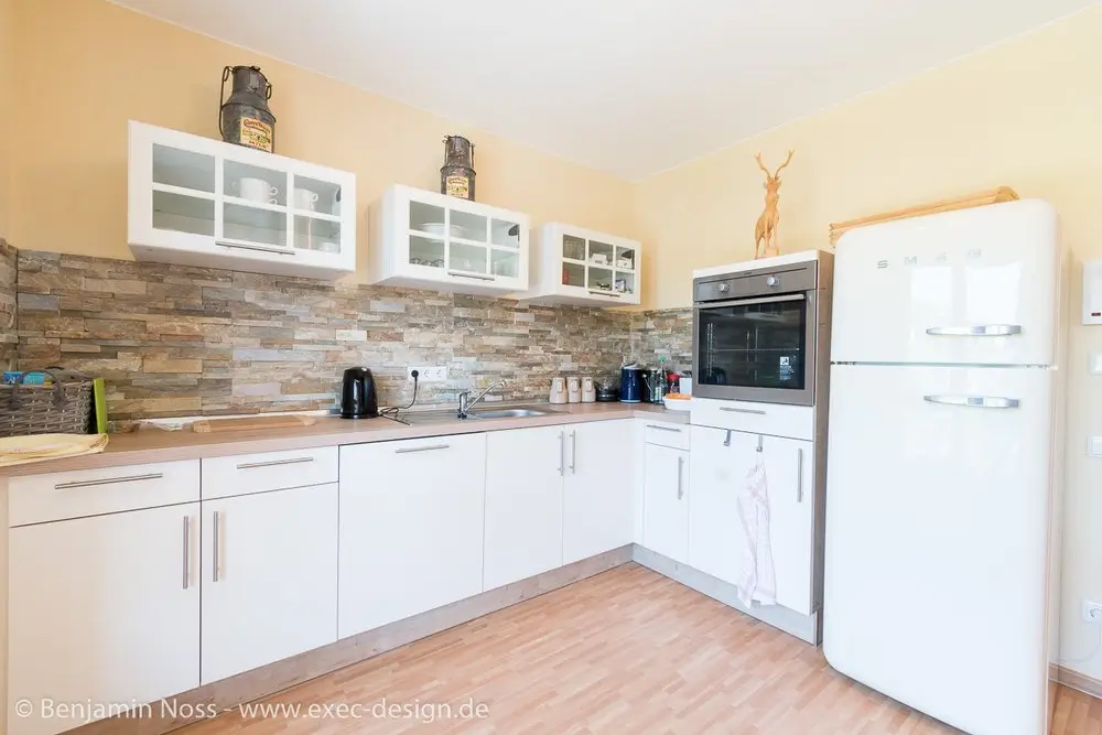 Moderne Küchenzeile mit weißen Schränken, Holzarbeitsplatte, eingebautem Backofen und weißem Retro-Kühlschrank